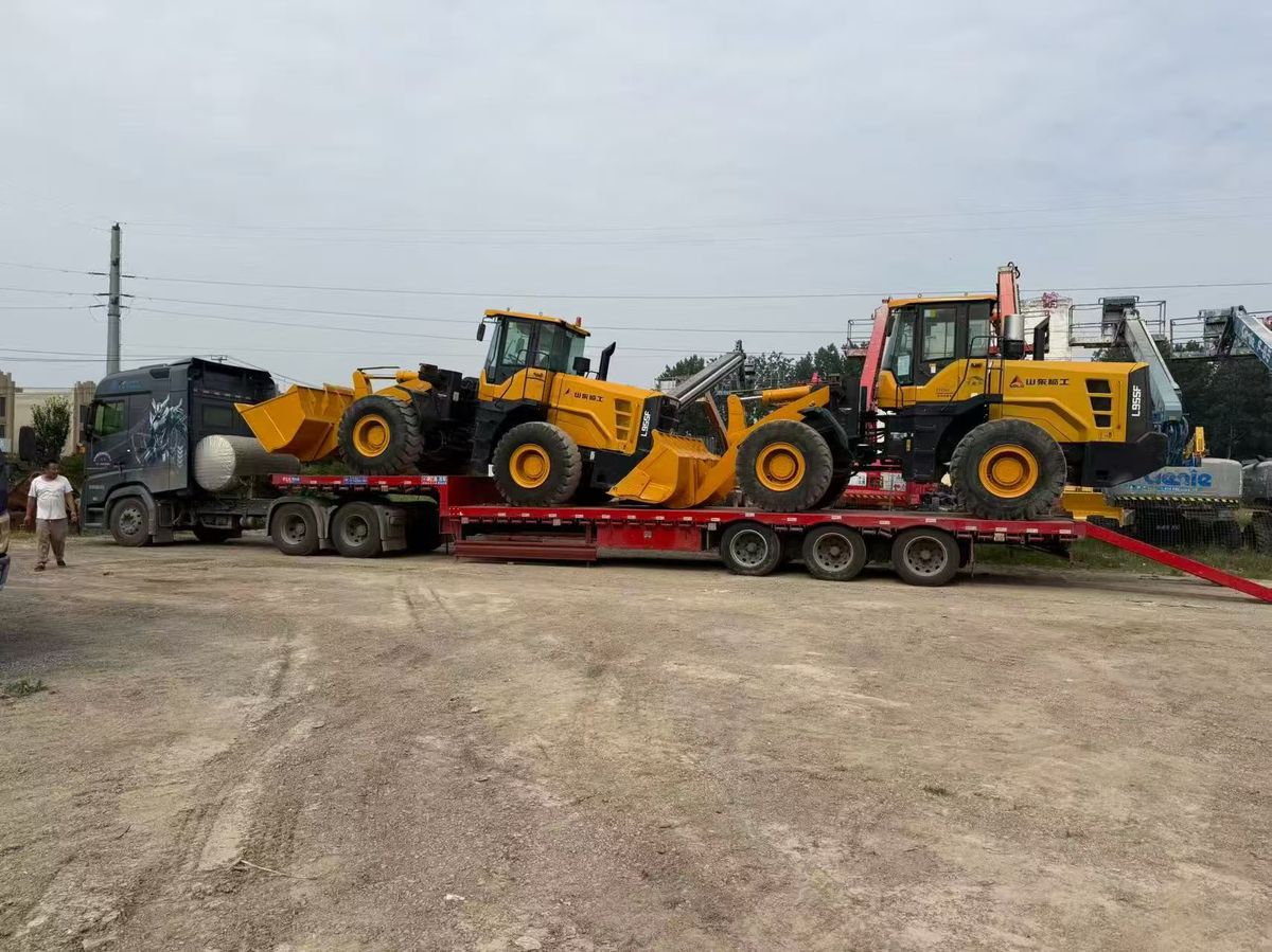 Wheel loaders on a low-bed trailer beside a tractor truck